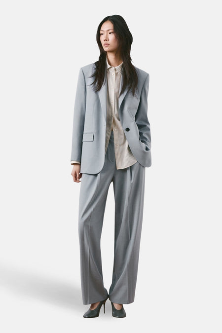 Pantalon de costume bleu de MANGO, coupe droite, porté avec une chemise rayée et des escarpins.
