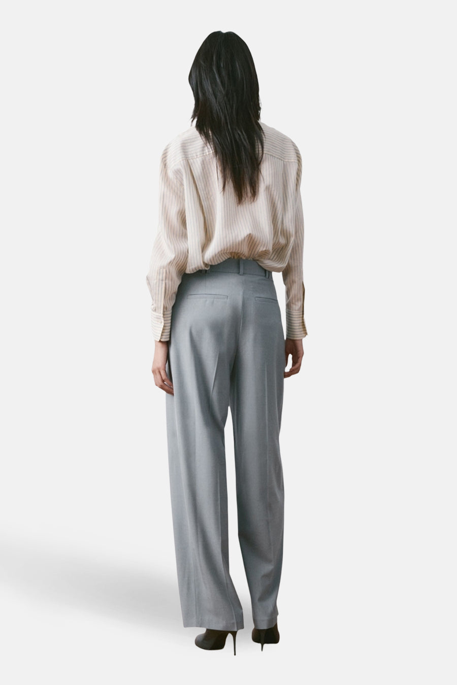Pantalon de costume bleu par MANGO, coupe ample, avec une chemise rayée et des chaussures à talons aiguilles.