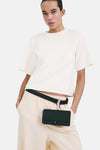 Pull col rond écru de MANGO, porté avec un pantalon couleur crème et une ceinture avec un petit sac attaché.
