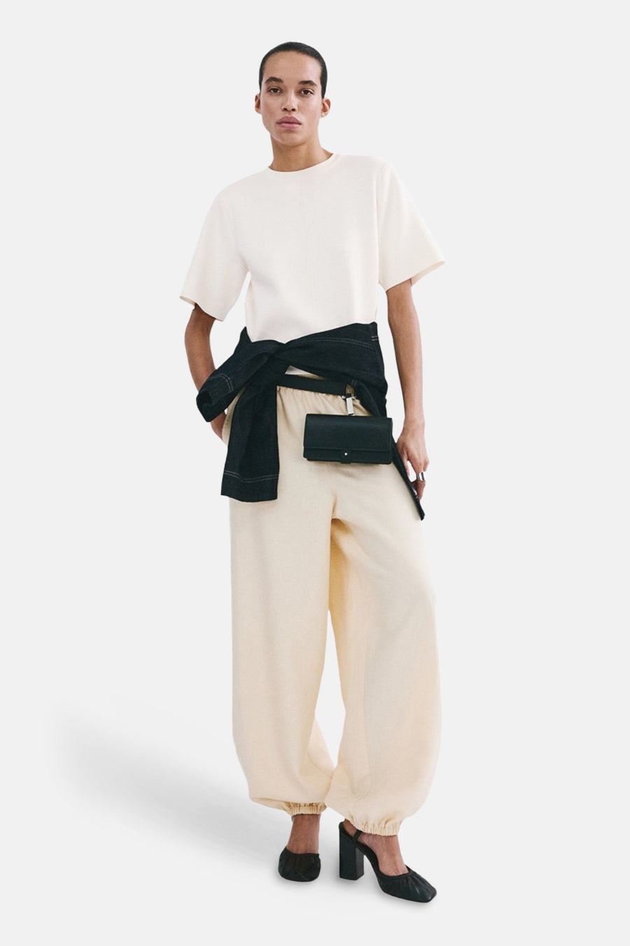 Pull écru col O de MANGO, porté avec un pantalon ample et des chaussures à talons noires.
