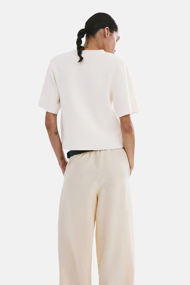 Pull col rond écru de MANGO, manches courtes, texture tricotée, porté avec un pantalon ample.