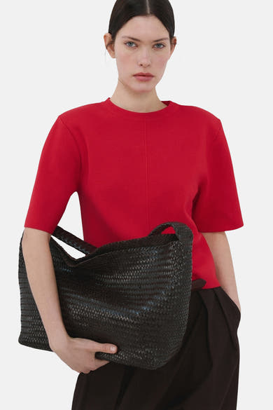 Pull rouge de MANGO, porté avec un pantalon foncé et un sac tressé.