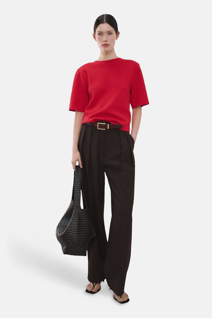 Pull rouge col O de MANGO, porté avec un pantalon large marron, une ceinture et un sac tissé noir.
