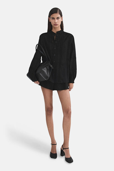 Chemisier noir à manches longues de MANGO, porté avec un short et des talons hauts noirs.