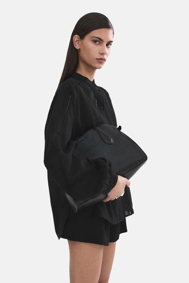 Chemisier noir à manches longues de MANGO, porté avec un sac à main noir assorti.