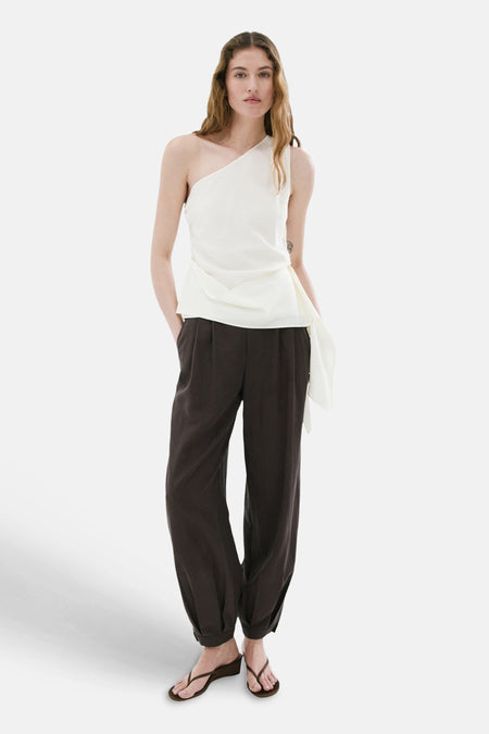 Blouse blanche asymétrique de MANGO avec un drapé fluide, portée avec un pantalon foncé.