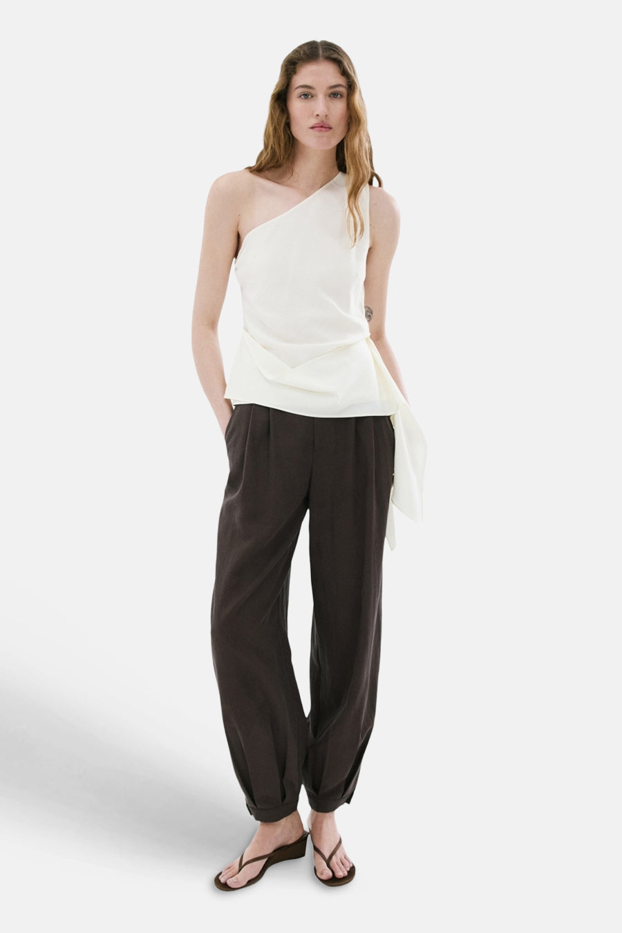 Asymmetrische witte blouse van MANGO met een vloeiende draperie, gedragen met een donkere broek.
