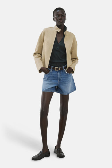 Bermuda en denim bleu moyen de MANGO, porté avec une veste beige, un polo vert foncé et des mocassins noirs.
