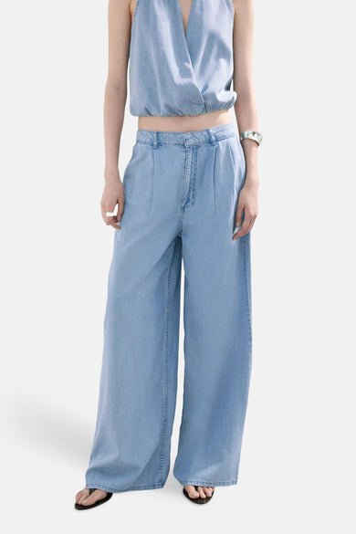 Light blue wide-leg denim pants with front pleats and classic stitching, worn with a matching top and black sandals, full-length front view