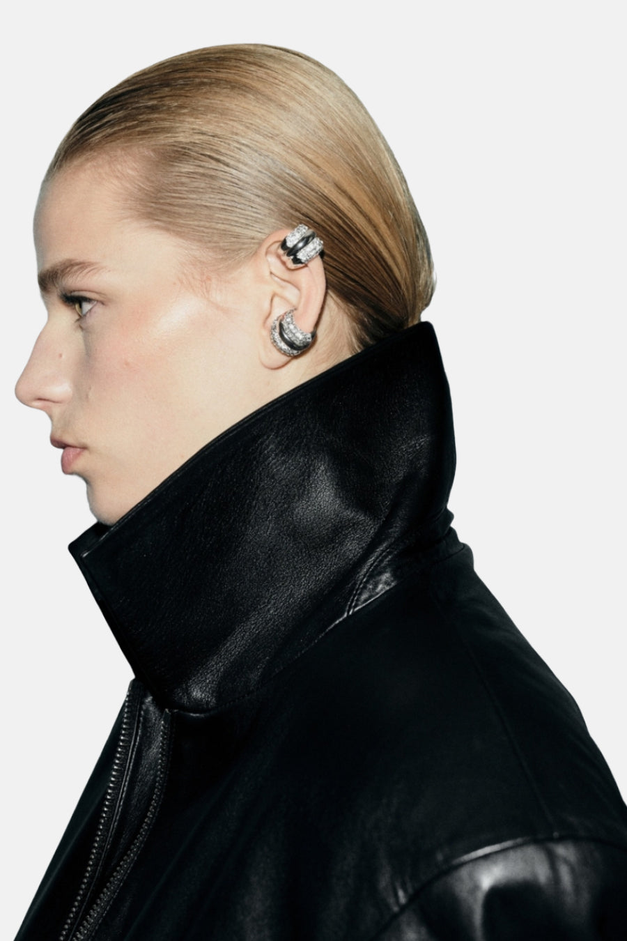 Boucles d'oreilles argentées de MANGO, ornées de strass, portées avec une veste en cuir noir.
