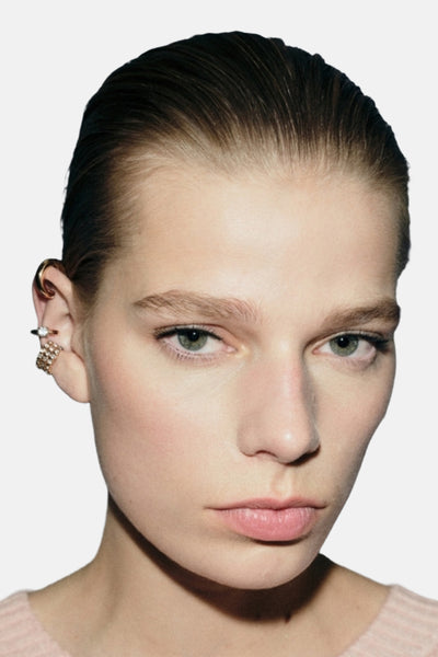 Boucles d'oreilles dorées de MANGO, portées par un mannequin avec des cheveux tirés en arrière et un pull rose pâle.