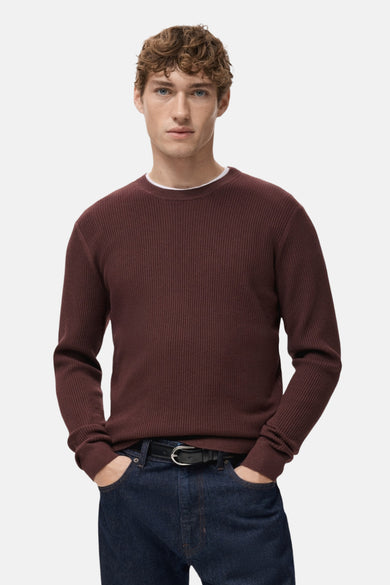 Pull à col rond bordeaux de MANGO avec texture côtelée, porté avec un jean foncé et une ceinture noire.