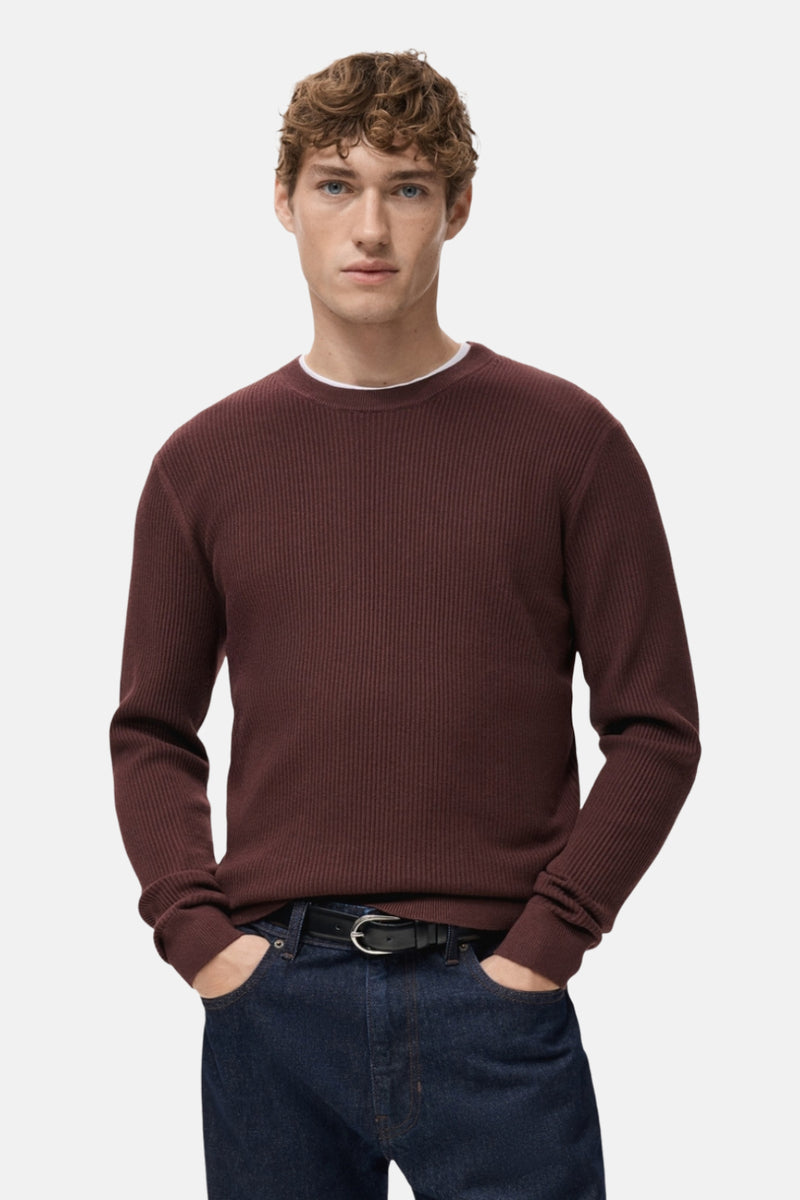 Pull à col rond bordeaux de MANGO avec texture côtelée, porté avec un jean foncé et une ceinture noire.