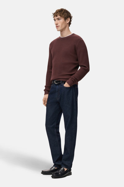 Bordeaux ronde hals trui van MANGO, in ribgebreide stof, gedragen met een donkere spijkerbroek en zwarte loafers.