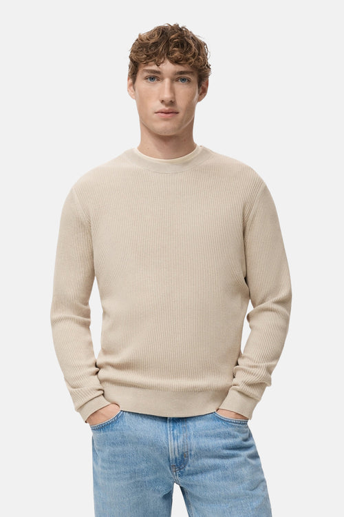 Pull à col rond beige de MANGO, en tricot côtelé, porté avec un jean bleu décontracté.