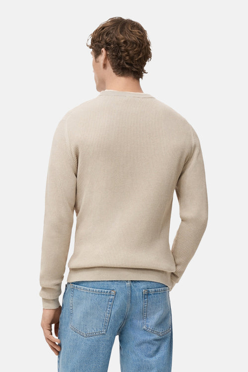 Pull à col rond beige de MANGO, avec une texture côtelée, porté avec un jean bleu clair, vue de dos.