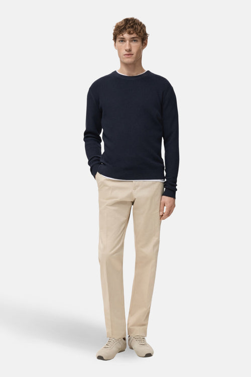 Pull à col rond bleu de MANGO, porté avec un t-shirt blanc et un pantalon beige avec des baskets ton sur ton.