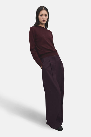 Pantalon bordeaux de MANGO, ample et à plis, porté avec un pull bordeaux assorti.