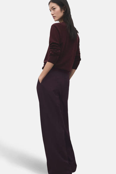 Pantalon bordeaux par MANGO, ample et fluide, avec poches latérales et porté avec un pull bordeaux.