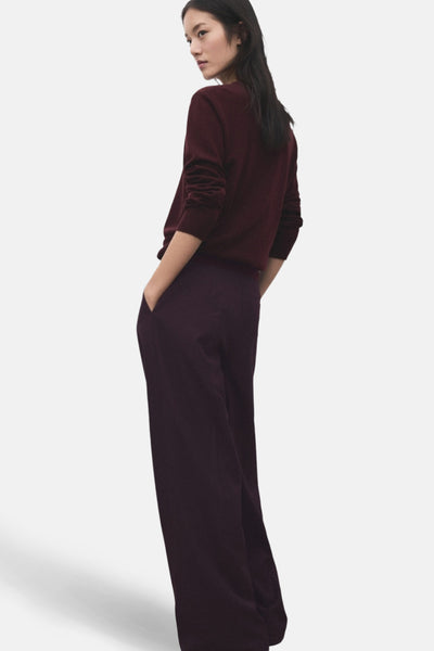 Pantalon bordeaux par MANGO, ample et fluide, avec poches latérales et porté avec un pull bordeaux.