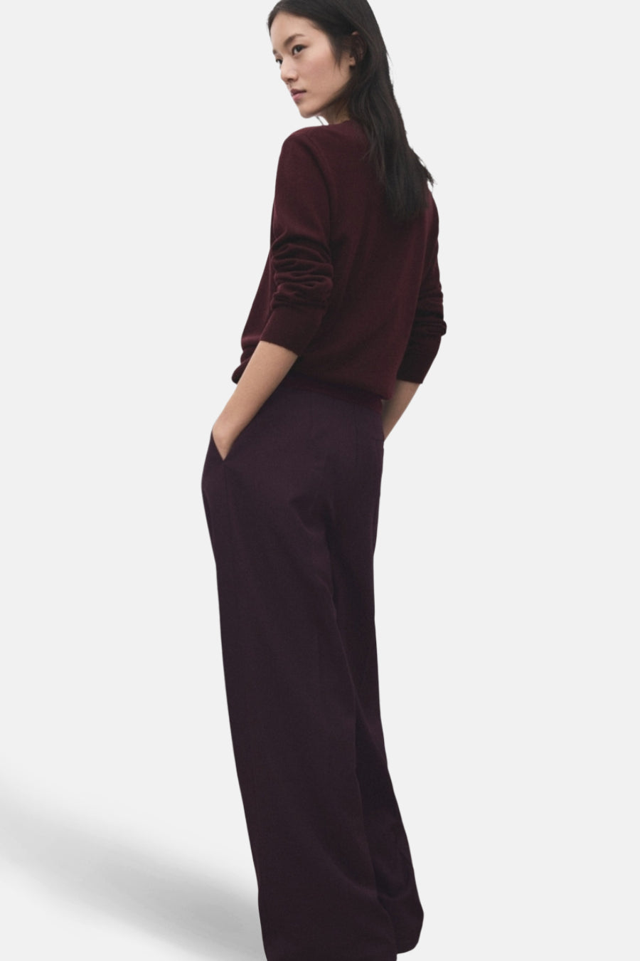 Pantalon bordeaux par MANGO, ample et fluide, avec poches latérales et porté avec un pull bordeaux.