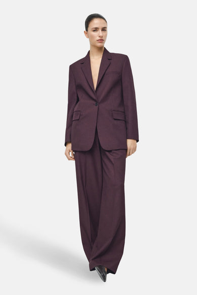 Bordeaux blazer van MANGO, gedragen met een bijpassende broek met wijde pijpen, op een witte achtergrond.