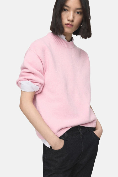 Pull ras du cou rose de MANGO porté sur une chemise blanche avec un jean foncé.