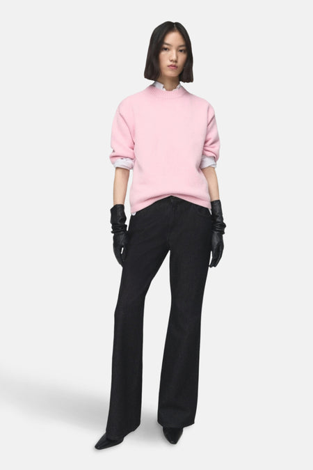 Pull à col rond rose de MANGO, porté avec un jean noir évasé, des gants en cuir et une chemise blanche.