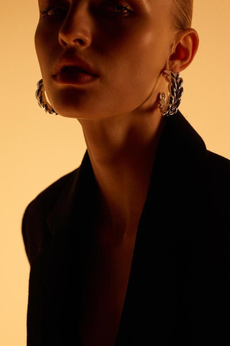 Boucles d'oreilles argentées tressées de MANGO, portées avec une veste noire et un fond neutre.