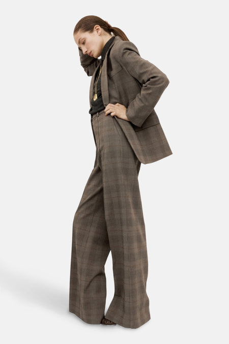 Pantalon marron à carreaux de MANGO, coupe ample, porté avec un pull noir et un collier doré.