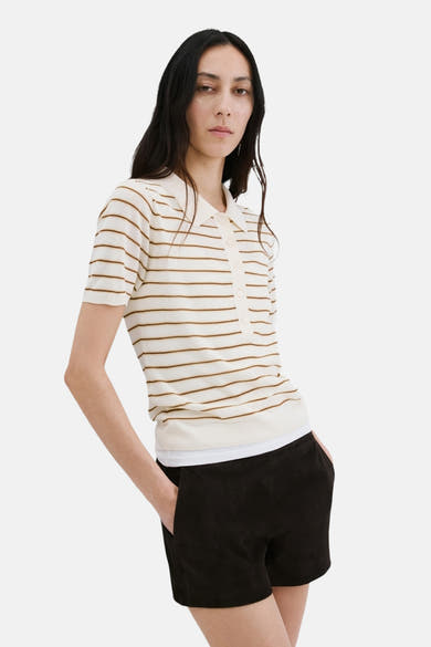 Beige polo met bruine strepen van MANGO, met een zwarte korte broek met zakken en donker haar.