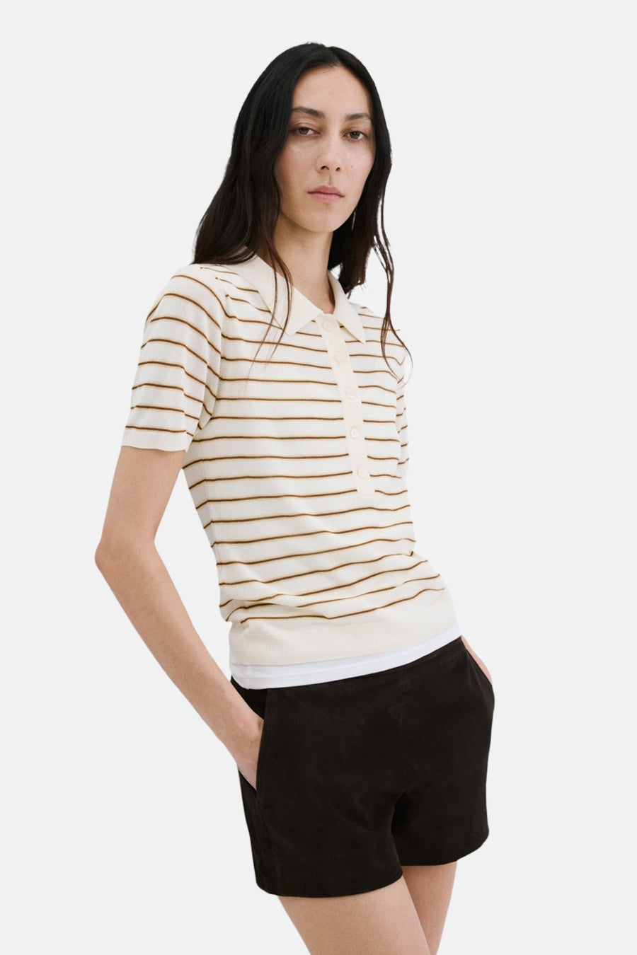 Beige polo met bruine strepen van MANGO, met een zwarte korte broek met zakken en donker haar.