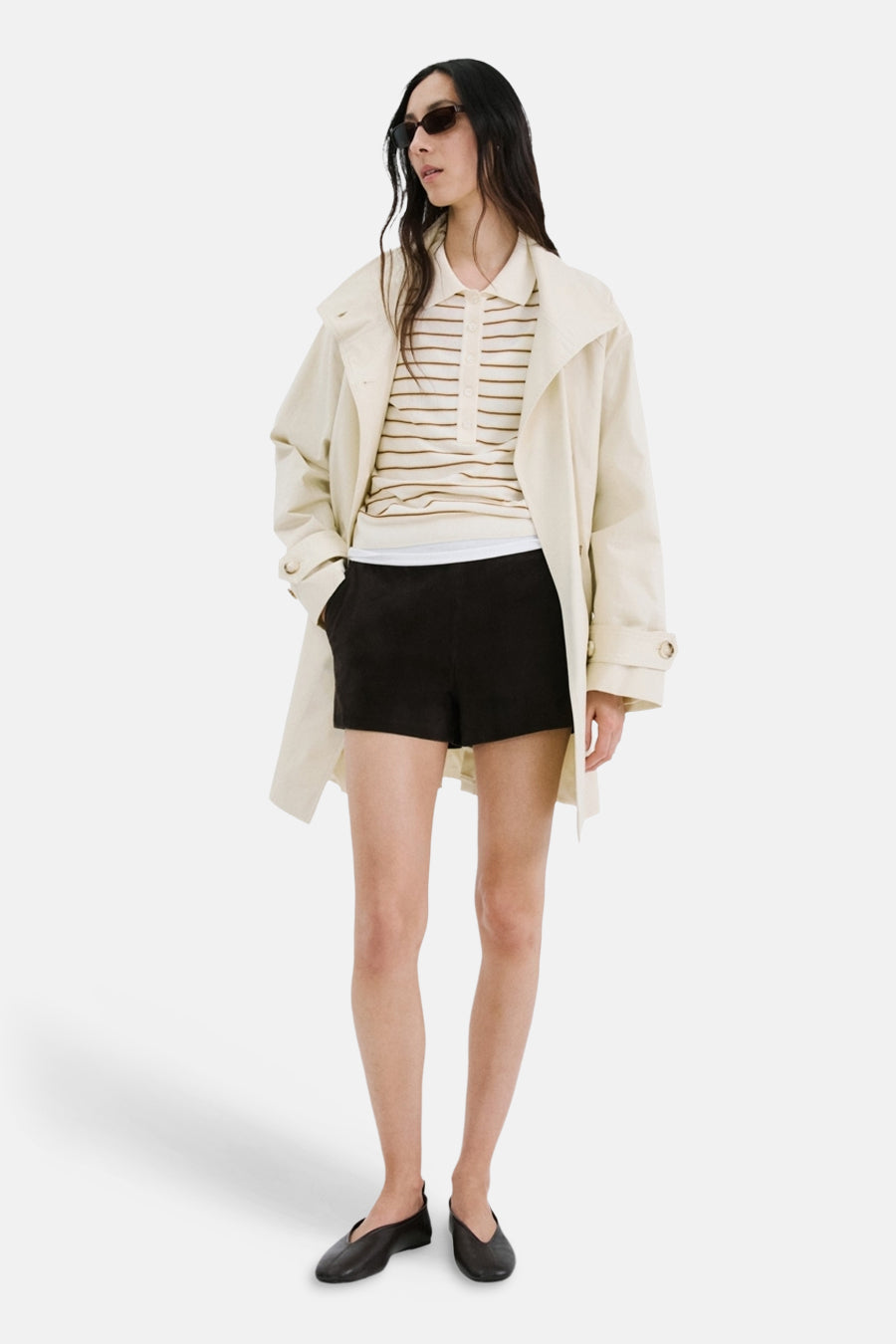 Beige gestreepte polo van MANGO gedragen met een trenchcoat, een zwarte korte broek en platte schoenen.