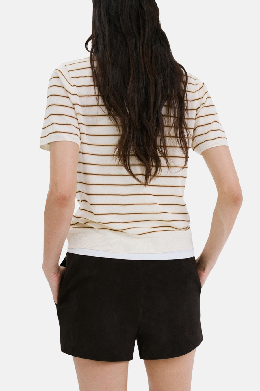 Polo beige à rayures marron de MANGO, avec un short noir à poches et une chevelure sombre.
