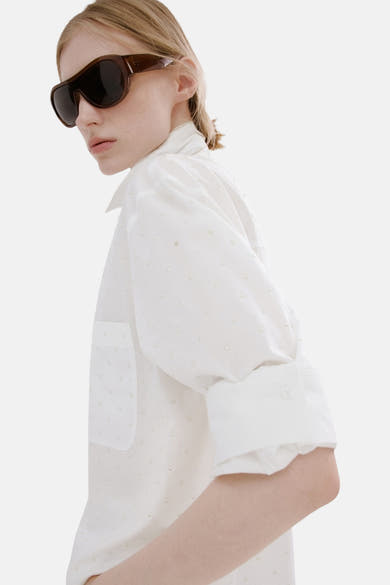 Witte blouse met lange mouwen van MANGO, gedragen met een witte broek, achterzijde, blond haar opgestoken.