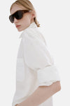 Witte blouse met lange mouwen van MANGO, gedragen met een witte broek, achterzijde, blond haar opgestoken.