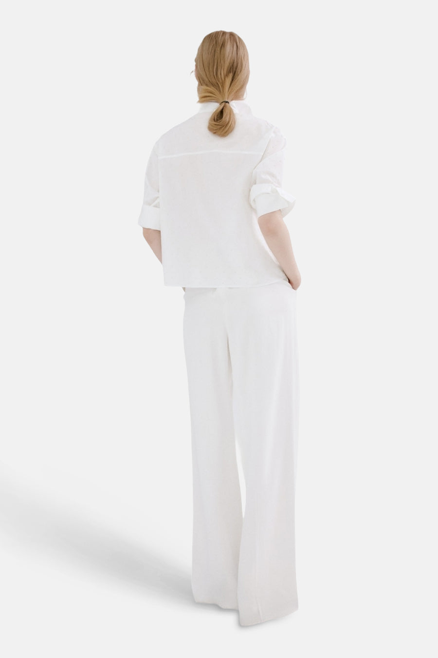 Chemisier à manches longues blanc de MANGO, porté avec un pantalon blanc, vue de dos, cheveux blonds attachés.