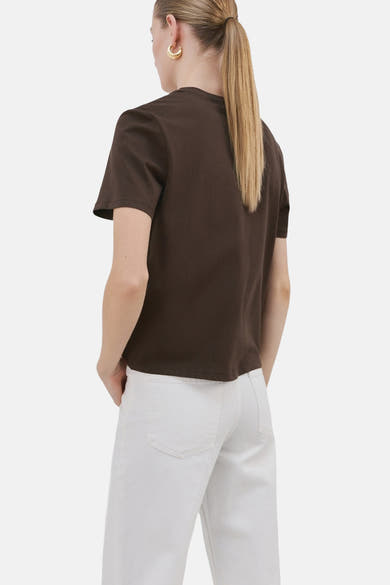 T-shirt brun à manches courtes de MANGO, porté avec un pantalon blanc taille haute et des boucles d'oreilles dorées.