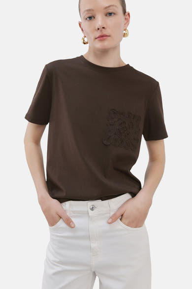 Bruin T-shirt met korte mouwen van MANGO, met geborduurde zak, gedragen met een witte broek.