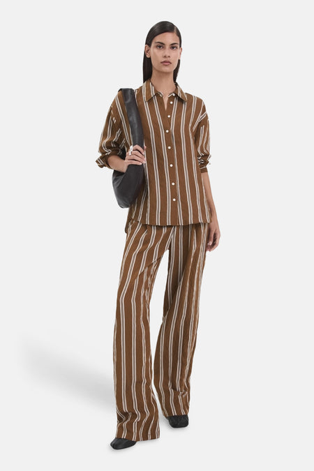 Chemise à manches longues brune à rayures blanches de MANGO, portée avec un pantalon assorti et un sac à bandoulière noir.