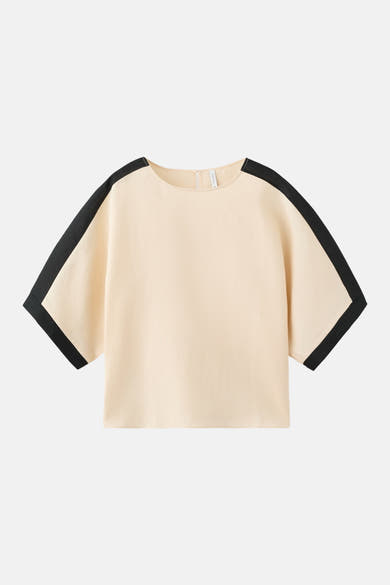 Crèmekleurig blouse met korte mouwen van MANGO, met zwarte bies aan de mouwen en schouders, gedragen met een bijpassende short.