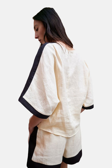 Chemisier à manches courtes crème de MANGO, avec bordure noire aux manches et aux épaules, porté avec un short assorti.
