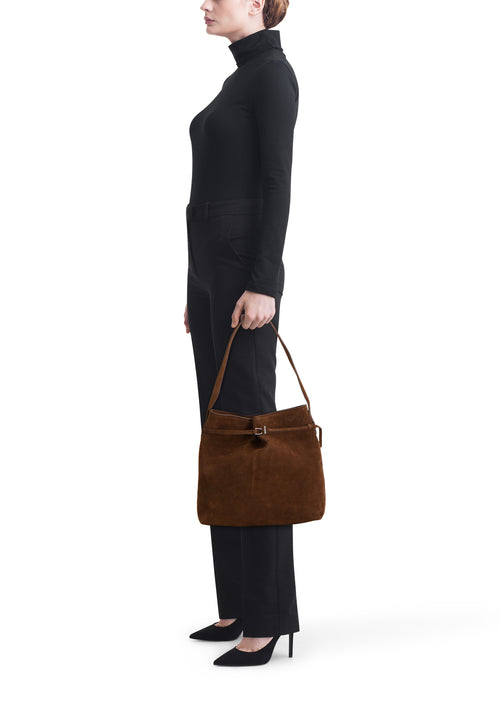 Bruine schoudertas van suède van MANGO, gedragen met een zwarte coltrui en een pantalon.