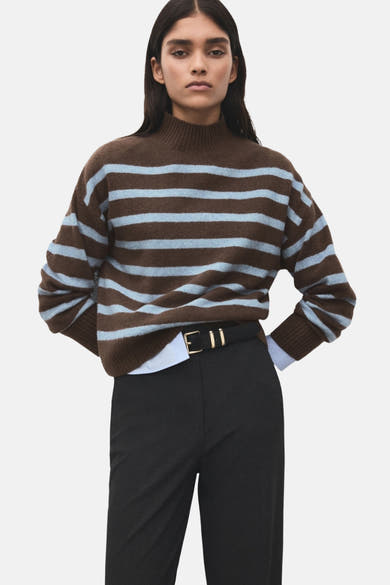 Pull à col rond multicolore de MANGO, à rayures marron et bleu clair, porté avec un pantalon noir et une ceinture noire.
