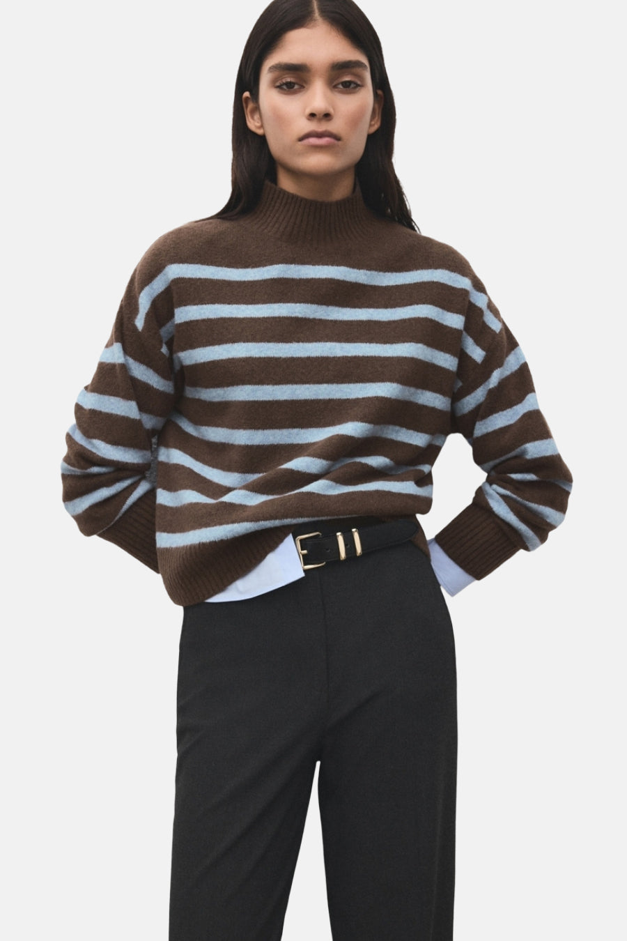 Pull à col rond multicolore de MANGO, à rayures marron et bleu clair, porté avec un pantalon noir et une ceinture noire.
