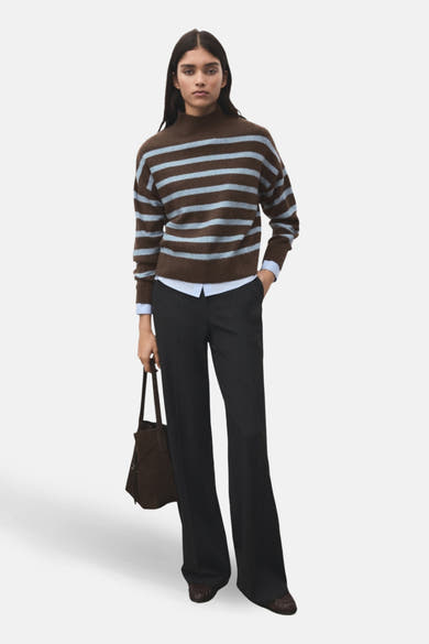 Pull à col rond multicolore de MANGO, à rayures horizontales, porté avec un pantalon sombre et un sac à main marron.