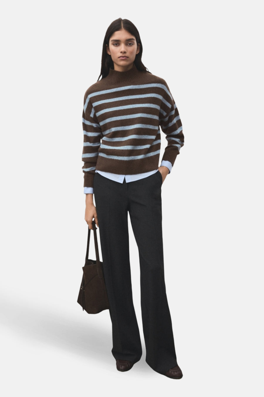 Pull à col rond multicolore de MANGO, à rayures horizontales, porté avec un pantalon sombre et un sac à main marron.