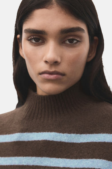 Pull à col rond marron et bleu clair de MANGO, porté par une femme, avec des rayures horizontales.
