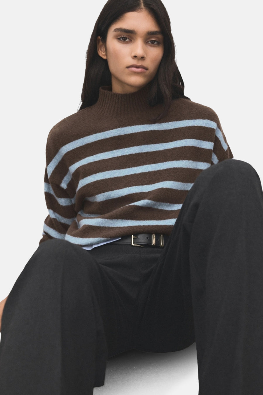 Pull à col rond marron rayé by MANGO avec des rayures bleu clair, porté avec un pantalon noir et une ceinture en cuir noir.