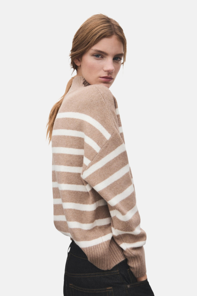 Pull à col rond beige de MANGO avec rayures blanches horizontales, porté avec un jean noir.